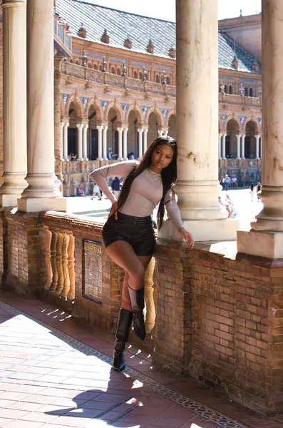 Deri şort, siyah çizme ve bej bluz giyen genç ve güzel Afrikalı kadın Seville 'de tatilde ve İspanya' nın ünlü meydanının tadını çıkarıyor. Seyahat ve tatil konsepti