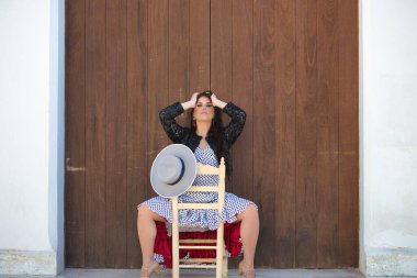 Latin kadın, genç ve güzel, dans eden flamenko, eski bir tahta sandalyede oturuyor. Kadın, siyah benekli, kısa siyah ceketli, beyaz bir elbise giyiyor.