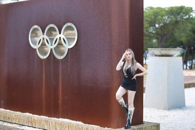 Açık renk gözlü, genç ve güzel bir kadın paslı metalin arka planında kendini beğenmiş, çelikten olimpiyat yüzükleri takan.