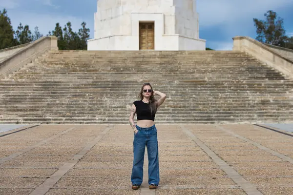 Genç ve güzel sarışın kadın, dövmeli ve kot pantolon giyiyor, siyah gömlek ve güneş gözlüğü takıyor, farklı pozlar veriyor ve farklı ifadeler takınıyor.