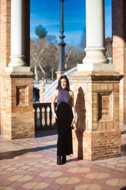 Zarif siyah elbiseli genç ve güzel esmer kadın Seville, Endülüs 'te İspanya' nın ünlü meydanında. Kadın mutlu ve mermer bir sütuna yaslanıyor.