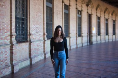 Esmer bir kadın, kot pantolon giymiş genç ve güzel ve siyah bir elbise giymiş Seville, Endülüs 'teki İspanya' nın ünlü meydanında yürüyor. Kadınlar anıtın tadını çıkarıyor.
