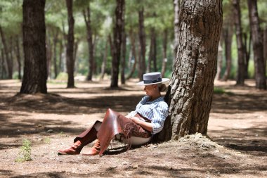 Genç, güzel bir kadın at kıyafetleri ve binicilik kıyafetleri giyer ve tipik bir İspanyol şapkası İspanya 'da kutsal bir günde bir çam ağacının gölgesinde dinlenir.