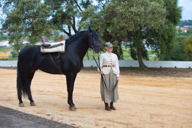 Genç ve güzel bir kadın Endülüs, İspanya 'da siyah safkan bir İspanyol atının dizginlerini tutuyor ve çekiyor. Kadın tipik bir atlı kadın kostümü giymiş.