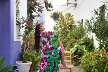 Flamenko dansı yapan genç ve güzel bir kadın, Endülüs 'ün tipik bir caddesinde bir ayağı yaşlı bir tahta sandalyede dinleniyor ve kafasını geriye atıyor. Fırfırlı bir elbise giymiş.