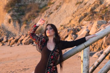 İspanyol kadın, esmer ve tipik flamenko dans kostümlü güzel flamenko dansçısı merdivenlerde sahile iniyor. Kayalık ve kayalar arka planda. Altın saatte fotoğraf çekimi.