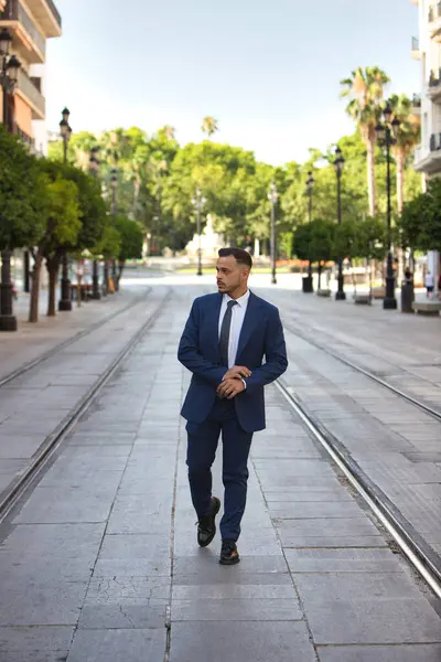 Genç, yakışıklı, koyu renk saçlı, takım elbiseli, kravatlı ve siyah dantelli ayakkabılı bir işadamı Seville 'de büyük bir caddede tramvay rayları arasında yürüyor. Adam çok uluslu bir şirketin yöneticisi.