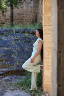 Uzun siyah saçlı güzel bir Latin genç, şehir dışındaki harabe bir şatonun taş duvarına yaslanıyor. Kadın kameraya bakıyor. Güzellik ve moda kavramı