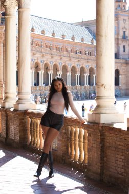 Deri şort, siyah çizme ve bej bluz giyen genç ve güzel Afrikalı kadın Seville 'de tatilde ve İspanya' nın ünlü meydanının tadını çıkarıyor. Seyahat ve tatil konsepti