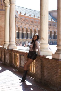 Deri şort, siyah çizme ve bej bluz giyen genç ve güzel Afrikalı kadın Seville 'de tatilde ve İspanya' nın ünlü meydanının tadını çıkarıyor. Seyahat ve tatil konsepti