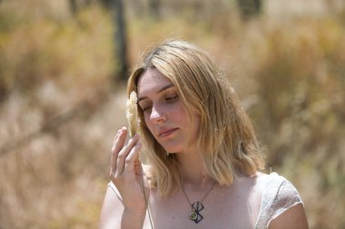 Genç, güzel sarışın bir kadının portresi. Huzurlu bir bakışla elinde kuru, yumuşak bir mısır kabuğu tutuyor ve narinlik ve şefkat ile yüzünün yanına yerleştiriyor.