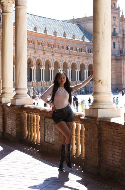 Deri şort, siyah çizme ve bej bluz giyen genç ve güzel Afrikalı kadın Seville 'de tatilde ve İspanya' nın ünlü meydanının tadını çıkarıyor. Seyahat ve tatil konsepti