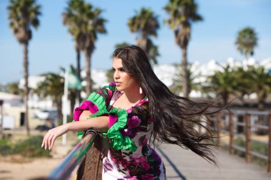 Latin bir kadın, genç ve güzel dans eden flamenko saçları havada elini ve kolunu korkuluklara uzatıyor. Dalgalı ve çiçekli beyaz elbiseli kadın tipik Endülüs.