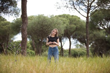 Genç ve güzel sarışın kadın, kot giyen, siyah gömlekli ağaçlar ve çiçekler arasında tarlada yürüyen. Kadın yalnızlığın ve ormanın bahar gününün tadını çıkarıyor.