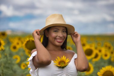 Beyaz gömlek ve hasır şapka giyen koyu tenli genç bir Latin kadın çiftçinin portresi ayçiçeklerinin arasında duruyordu. Kız şapkasını eliyle tutuyor ve göğsünde bir ayçiçeği var.