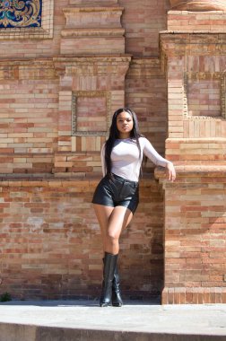 Genç, güzel Afrikalı kadın dirseğiyle İspanya 'nın Seville meydanındaki kare kırmızı tuğla bir sütunun üzerinde dinleniyor. Seyahat ve tatil konsepti