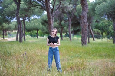Genç ve güzel sarışın kadın, kot giyen, siyah gömlekli ağaçlar ve çiçekler arasında tarlada yürüyen. Kadın yalnızlığın ve ormanın bahar gününün tadını çıkarıyor.