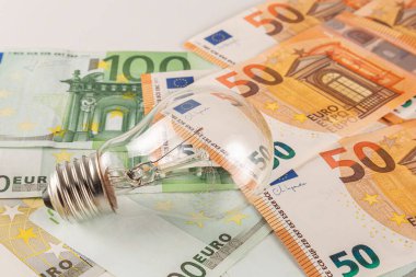 Arka planda büyük miktarda euro banknotuyla kaplı bir masanın üzerinde bir ampul bulunuyor.