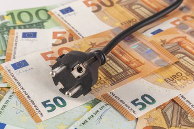 Yakın planda büyük miktarda euro banknotuyla kaplı bir masanın üzerindeki siyah bir elektrik prizi.
