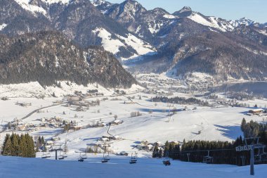 Walchsee village in a mountain valley on a sunny winter day with a ski lift in the foreground. Austria. clipart