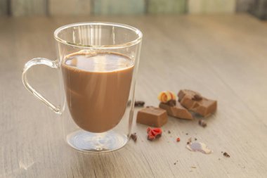 Bardakta çikolatalı süt ve tahta masada çikolata.