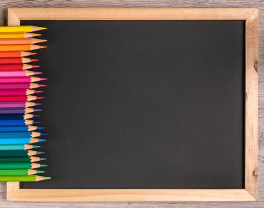 Keskin renkli kalemler, kopya alanı olan siyah bir tahtaya düzenli olarak dizilmiş. Kapatın, okul - ofis malzemeleri.