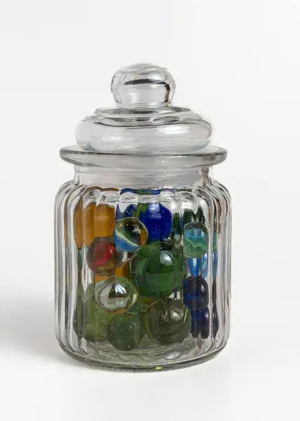 Beyaz arka planda cam bir kavanozda çok renkli misketler. Dikey.