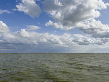 Bir yelkenlinin güvertesinden mavi gökyüzü, beyaz bulutlar ve uzaktaki sahile bakın..