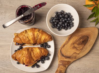 Kruvasan, reçel kavanozu ve ahşap masada taze yaban mersini. Üst görünüm.