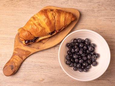 Tahtada reçel dolu kruvasan ve tahta yüzeyde taze yaban mersini dolu kruvasan.