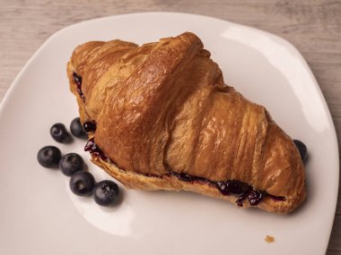 Reçelli kruvasan ve beyaz tabakta taze yaban mersini. Kapat..