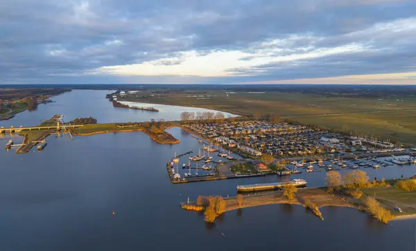 Bereketli yeşillik ve sudaki huzur yansımalarıyla çevrili tekneli sakin bir marinanın üzerinde altın bir günbatımı..