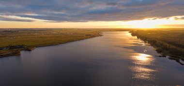 Sakin bir nehrin üzerinde gün batımı, sakin kırsal bölgeler ve engin açık manzaralarla çevrili altın yansımalarla. Hollanda, Nijkerk.