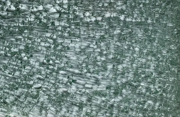 Kırık cam parçaları yeşil renkte. Keskin, yansıtıcı ve düzensiz şekillerden oluşan karmaşık bir mozaik oluşturuyor..