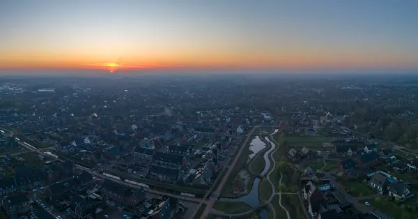 Nijkerk üzerinde panoramik bir gündoğumu manzarası, dolambaçlı yolları ve sabah ışığını yansıtan parıldayan bir nehri olan huzurlu bir yerleşim alanını gösteriyor..