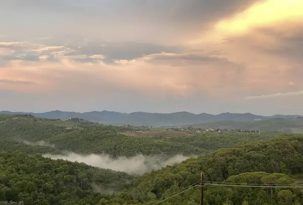 Sisli ormanlık tepelerde gün batımı ve sakin kırsal Tuscany 'de uzak dağlar.