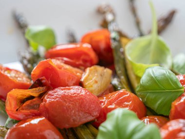 Renkli, sağlıklı bir tabak ızgara kuşkonmaz ve vişneli domates. Yaz vejetaryen yemeği için taze fesleğenle birlikte..