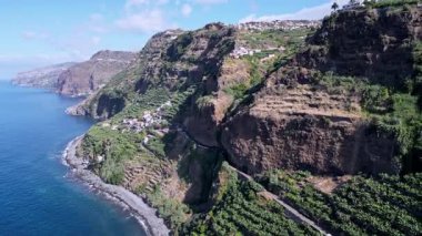 Teraslı uçurumlarla Madeira kıyı şeridi, yoldaki şelale, okyanus dalgaları ve yemyeşil yamaçlarda yuva yapmış köyler.