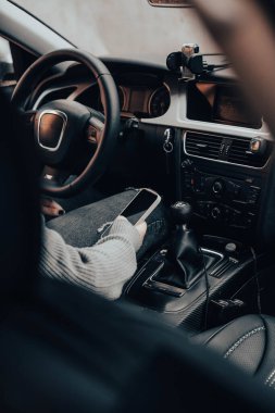 Genç kız arabayı temizliyor. Arabasında otururken telefonunu kullanan bir kız..