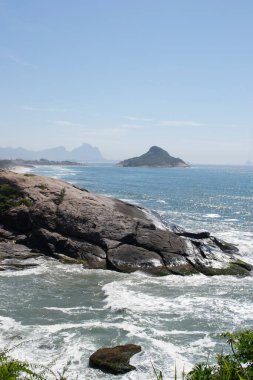 Rio de Janeiro şehrinde yer alan Praia do Pontal 'ın berrak mavi sularıyla dağların, bitki örtüsünün ve okyanusun panoramik manzarası.