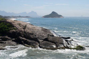 Rio de Janeiro şehrinde yer alan Praia do Pontal 'ın berrak mavi sularıyla dağların, bitki örtüsünün ve okyanusun panoramik manzarası.
