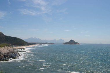 Rio de Janeiro şehrinde yer alan Praia do Pontal 'ın berrak mavi sularıyla dağların, bitki örtüsünün ve okyanusun panoramik manzarası.
