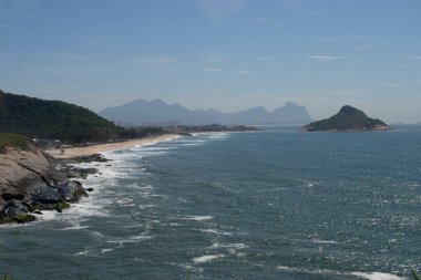 Rio de Janeiro şehrinde yer alan Praia do Pontal 'ın berrak mavi sularıyla dağların, bitki örtüsünün ve okyanusun panoramik manzarası.