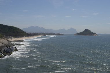 Rio de Janeiro şehrinde yer alan Praia do Pontal 'ın berrak mavi sularıyla dağların, bitki örtüsünün ve okyanusun panoramik manzarası.