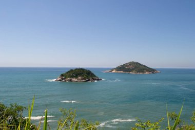 Rio de Janeiro şehrinde yer alan Praia de Grumari 'nin berrak mavi sularıyla dağlar, bitki örtüsü ve okyanus..