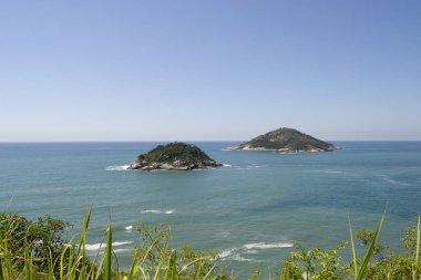 Rio de Janeiro şehrinde yer alan Praia de Grumari 'nin berrak mavi sularıyla dağlar, bitki örtüsü ve okyanus..
