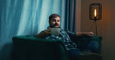 Man Drinking Coffee on a Green Soft Armchair. Relaxed Male Drinking Coffee. Coffee Drinking. Home. Green Sofa