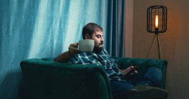 Man Drinking Coffee on a Green Soft Armchair. Relaxed Male Drinking Coffee. Coffee Drinking. Home. Green Sofa
