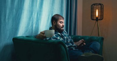 Man Drinking Coffee on a Green Soft Armchair. Relaxed Male Drinking Coffee. Coffee Drinking. Home. Green Sofa