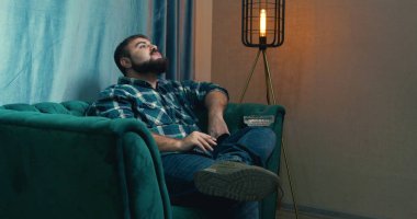 Man smoking cigarette on a green armchair, man checking social media via phone. handsome man smoking a cigarette. Lips blowing smoke. Adult bearded man smoking joint cigarette.